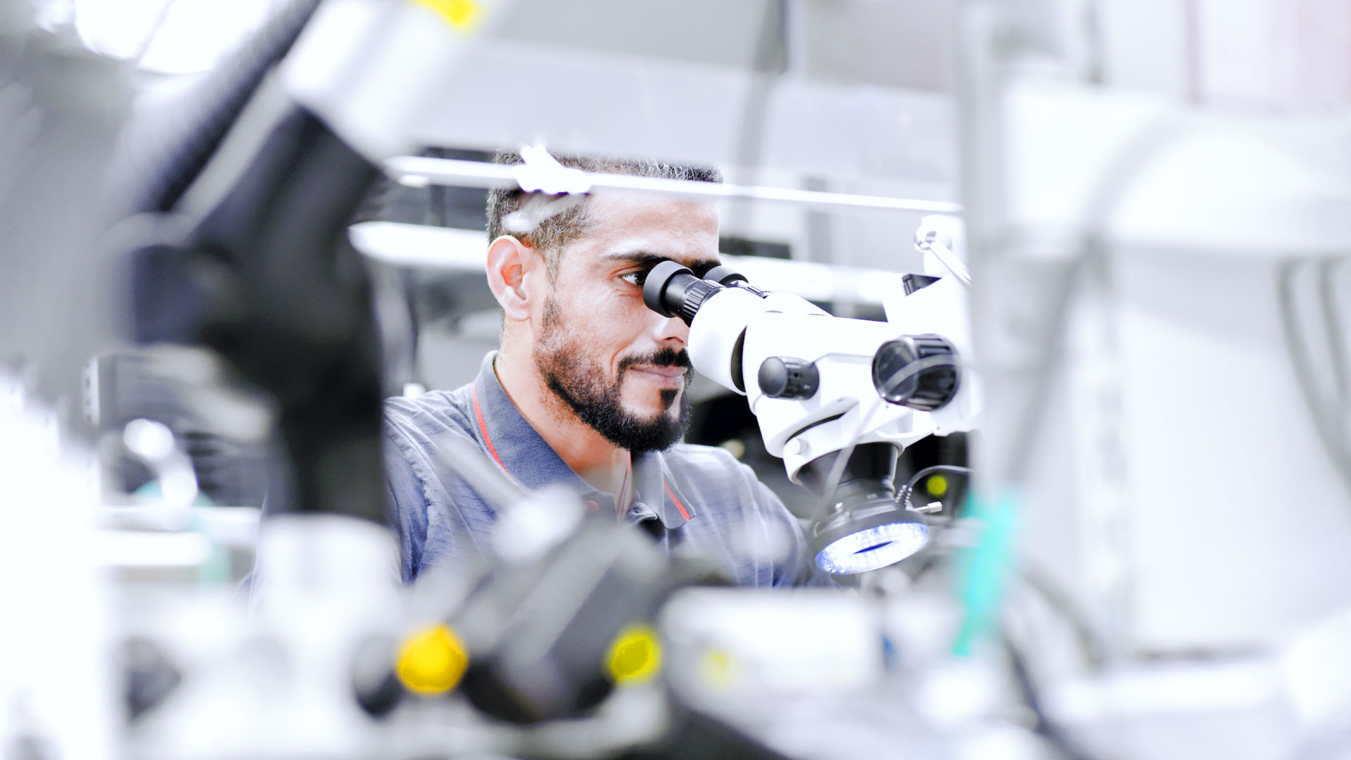 junger Mann an einem Mikroskop umgeben von technischer Ausstattung