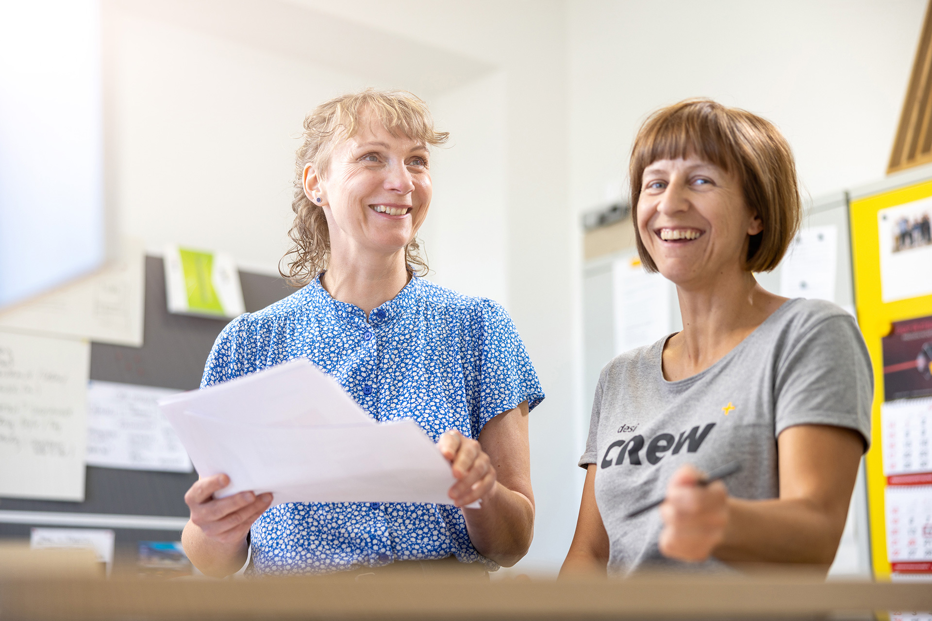 2 Mitarbeiterinnen der designerei lachen am Stehtisch